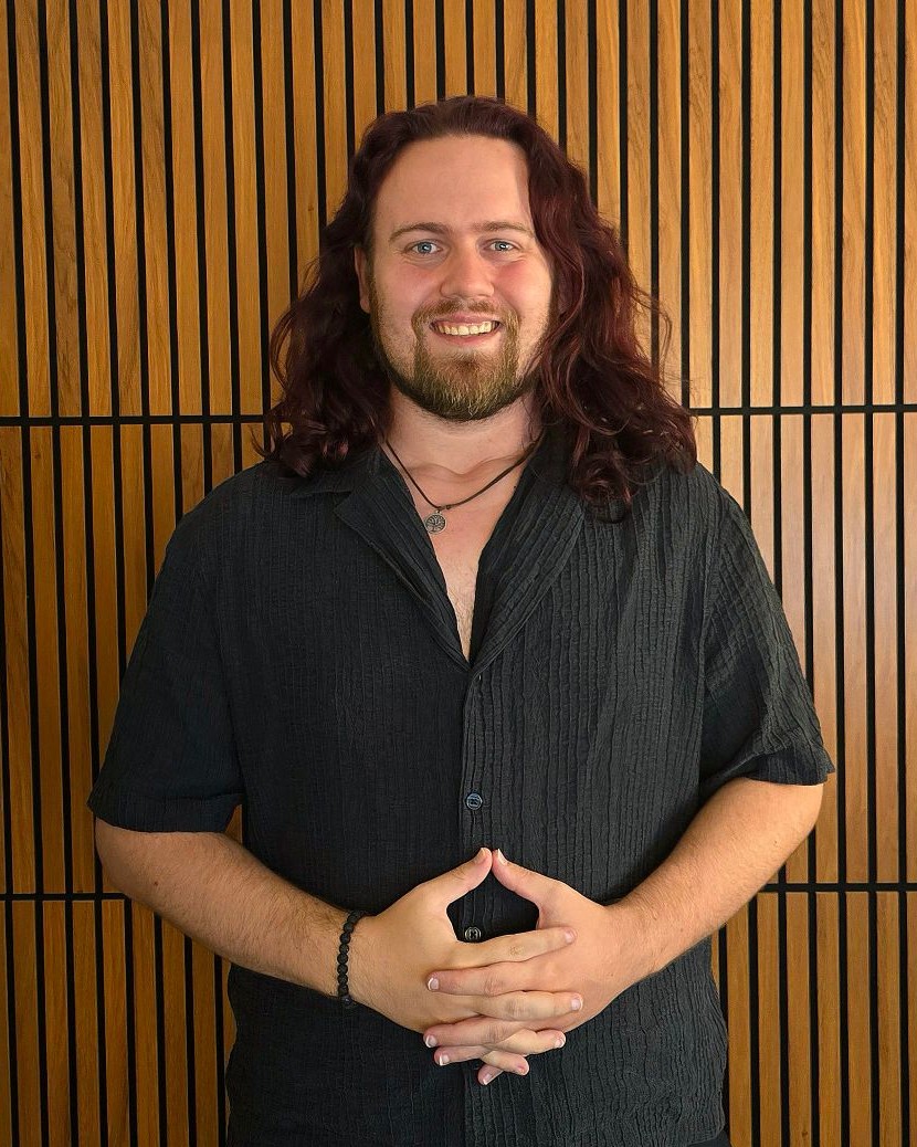 Porträt von Michael vor einer Holzwand, lächelnd, die Hände vor dem Körper gefaltet
